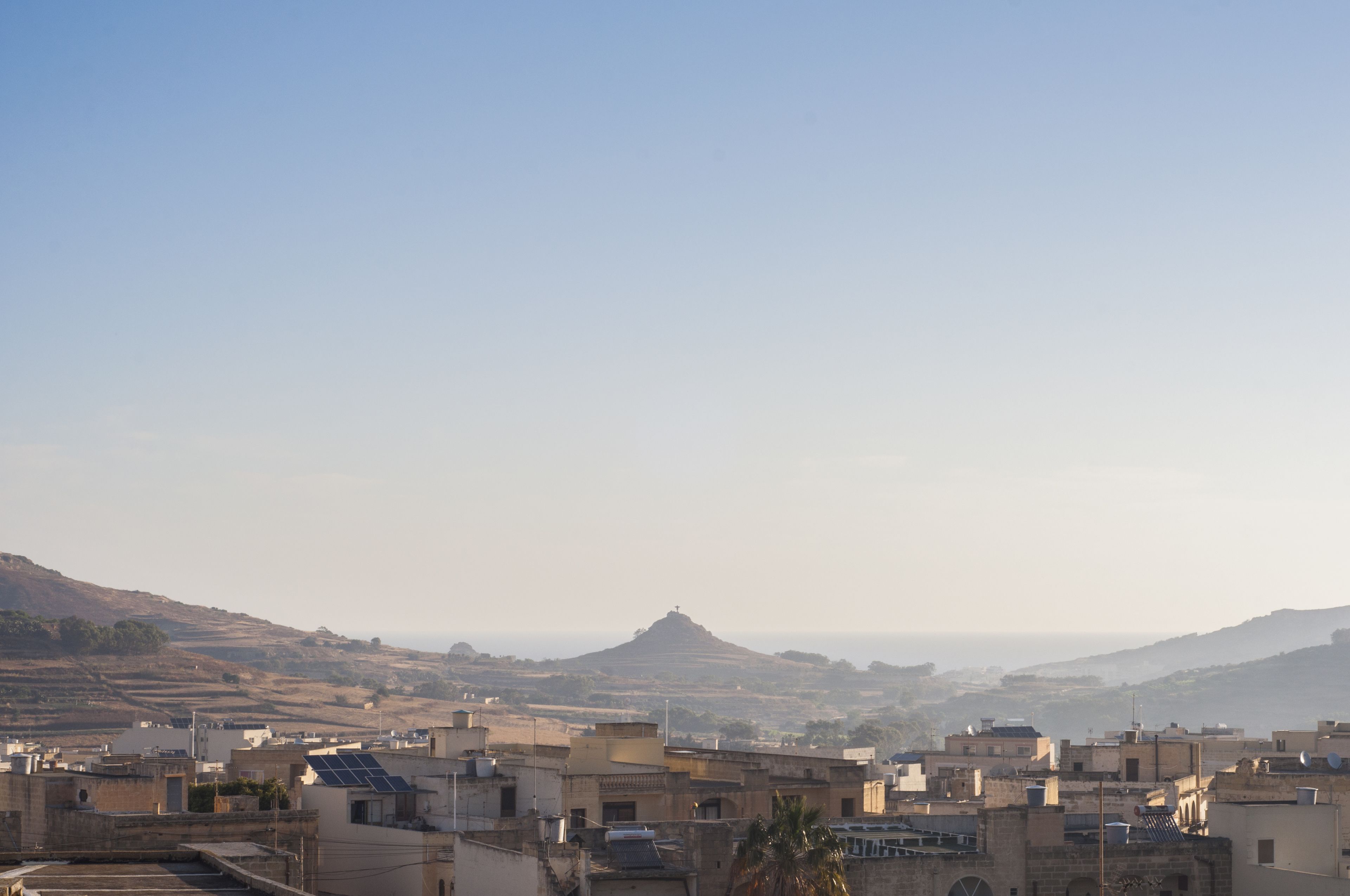 A cityscape with buildings, a hill, and a distant view of the sea.