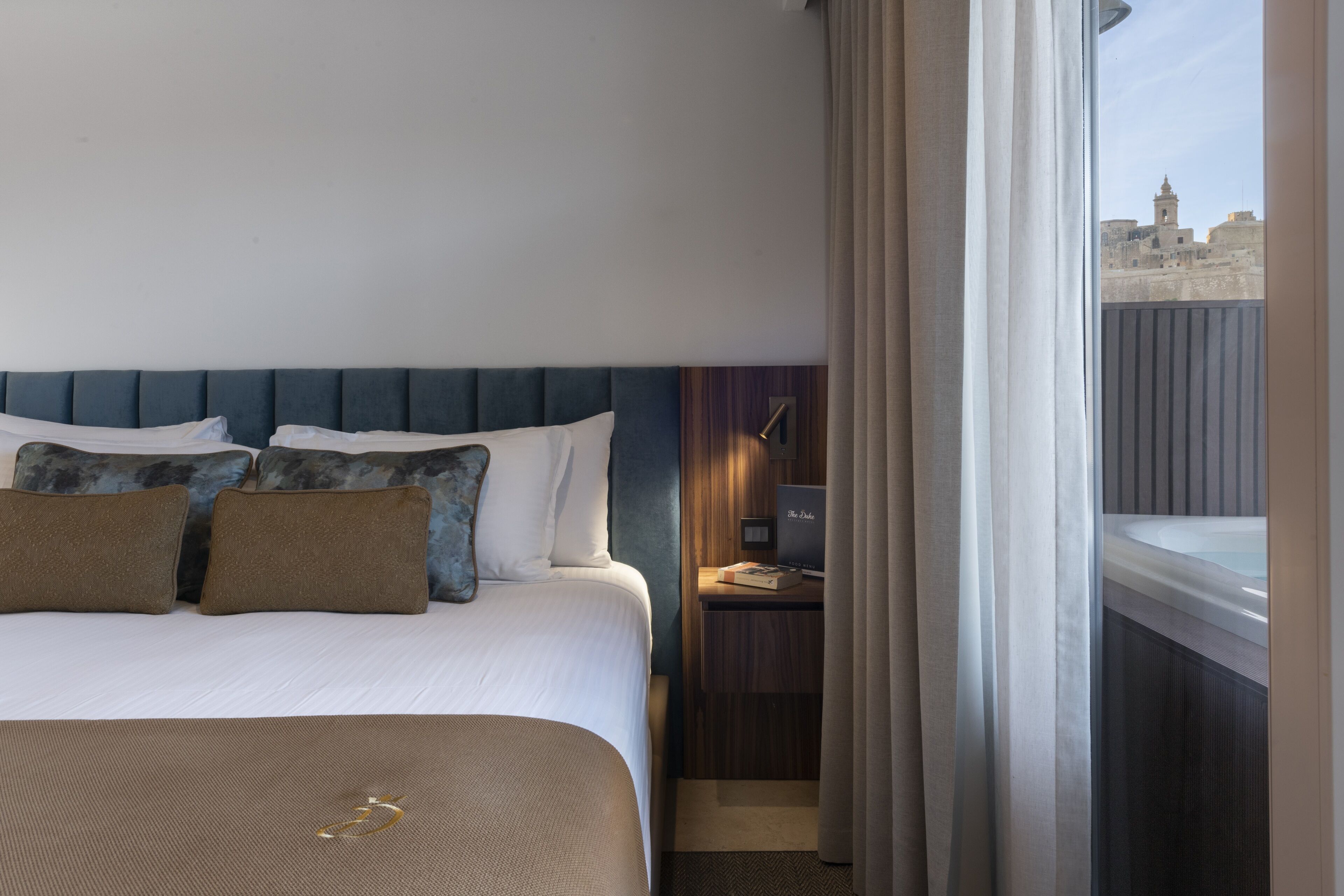 A hotel room with a bed, a nightstand, a laptop, and a view of a cityscape through a window.