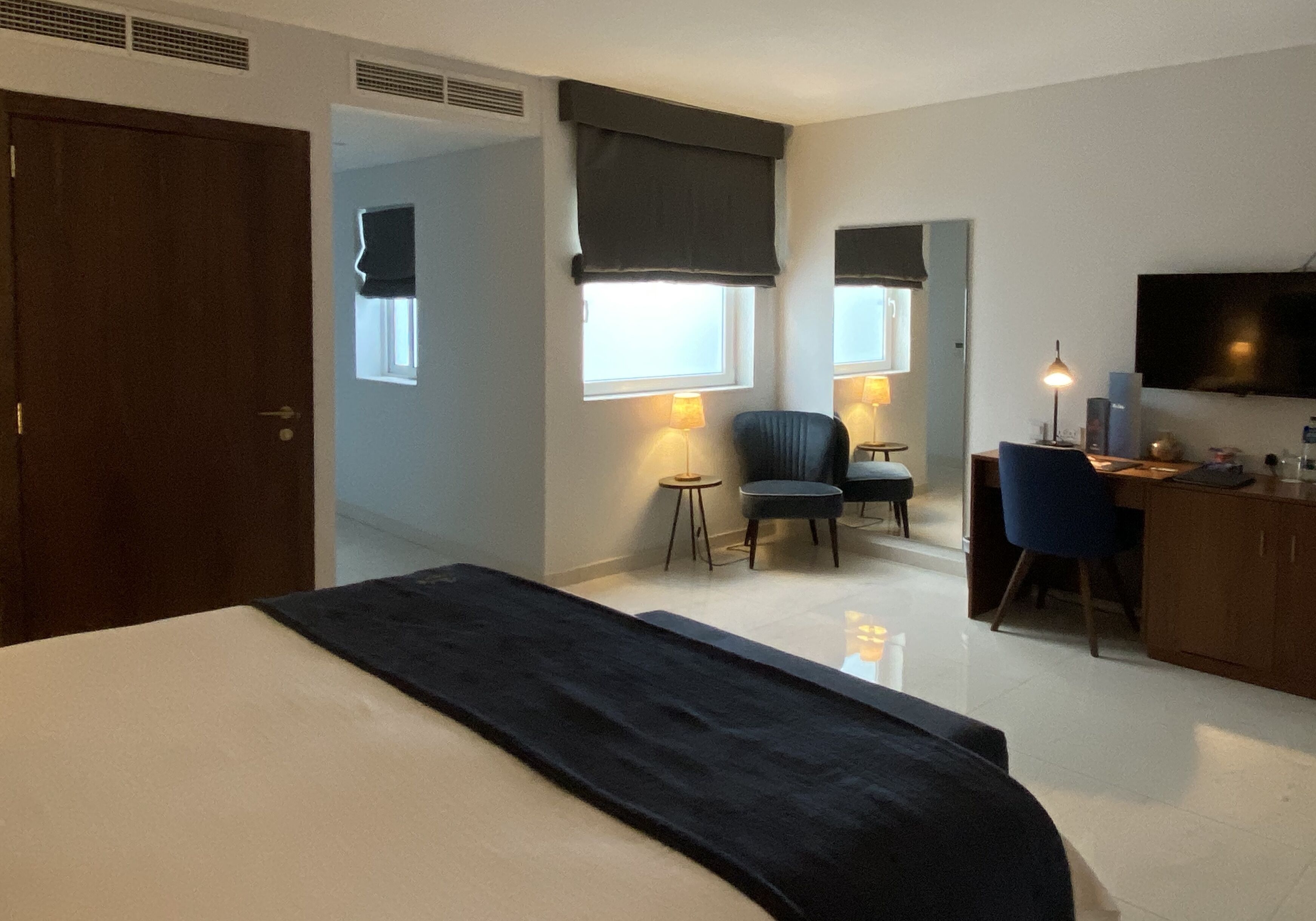 A hotel room with a bed, a desk with a chair, two lamps, a television, and a window with a view.