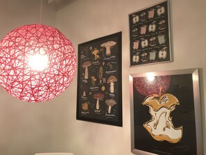 Una pared con tres obras de arte enmarcadas: un elemento de iluminación esférico rojo, una ilustración enmarcada de hongos y una ilustración enmarcada de manzanas.