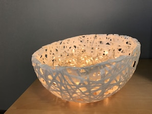 A white, intricately woven bowl with string lights inside, placed on a wooden surface against a dark background. - City Apartment (Jyväskylä)