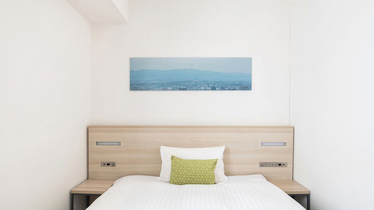 A hotel room with a bed, a nightstand, a wall-mounted picture, and a headboard.