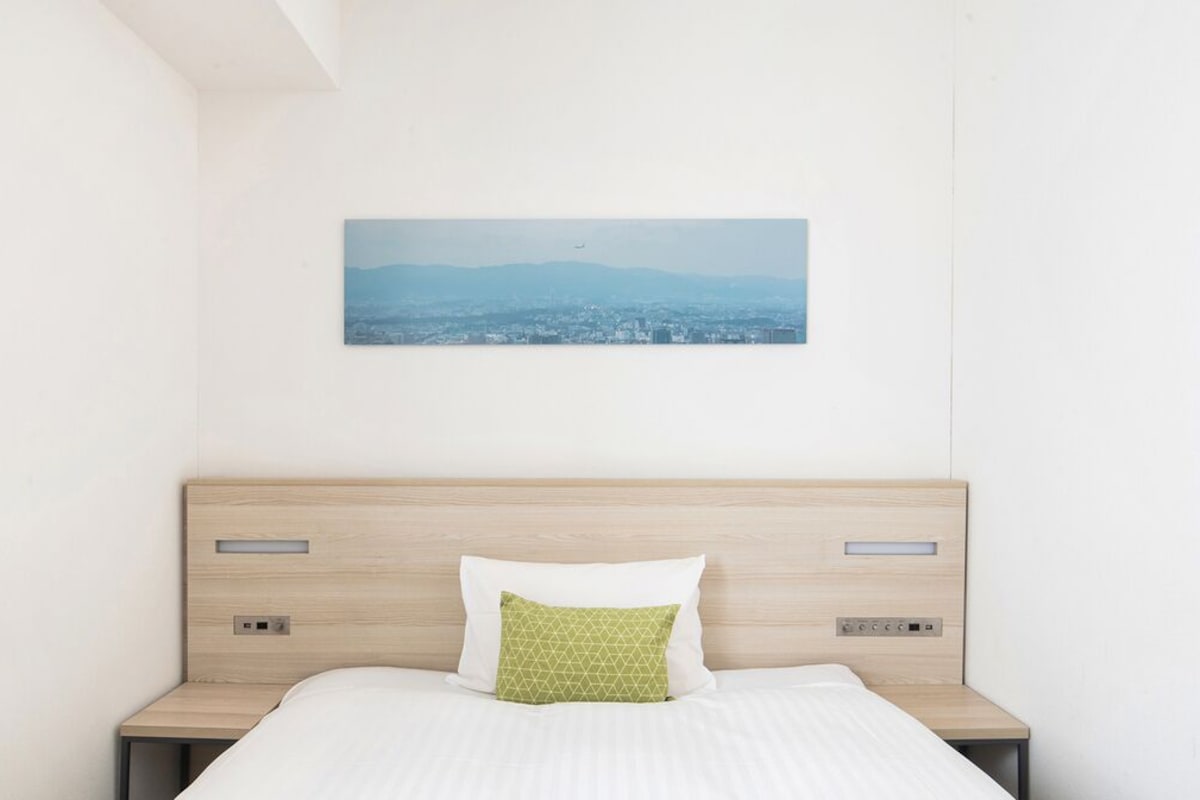 A hotel room with a bed, a nightstand, a wall-mounted picture, and a headboard.