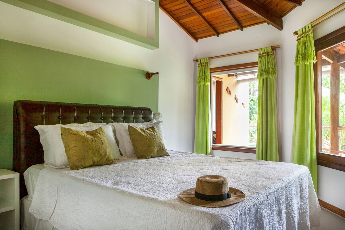 A neatly made bed with a white bedspread and a straw hat on it.