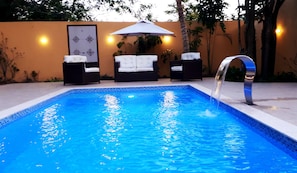 A swimming pool with a clear blue water feature, surrounded by lounge chairs and an umbrella. - Espaço do Sagui (Maraú)