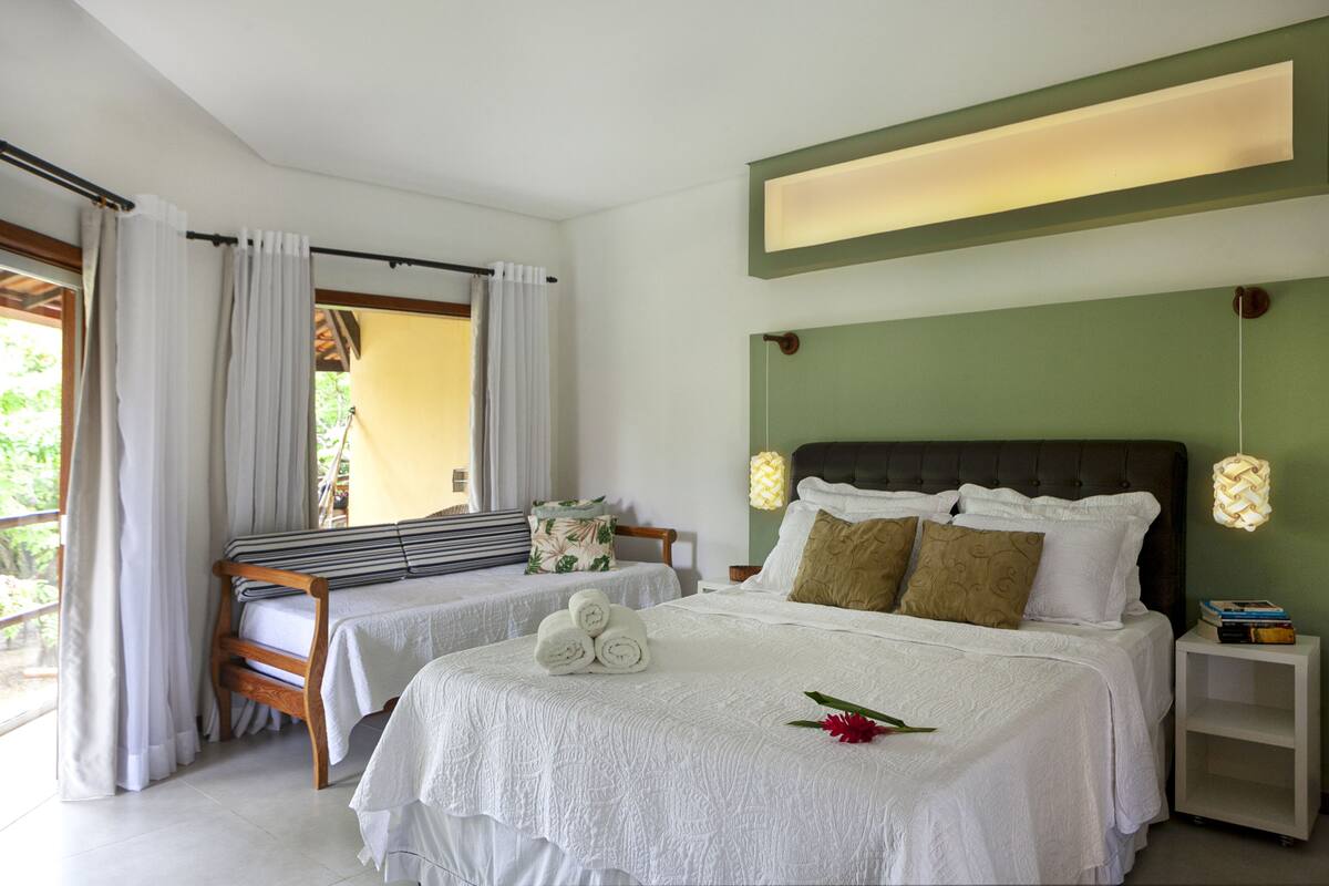 A hotel room with two beds, a wooden bench, a small table, and a nightstand with a lamp.