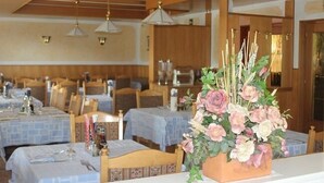 A dining area with tables set for guests, wooden ceiling beams, and hanging pendant lights. - Albergo Alla Posta (Pinzolo)