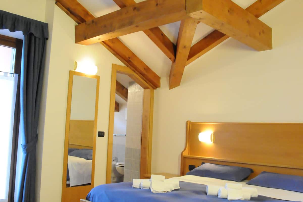 A bedroom with a wooden ceiling, a bed with blue bedding, and a mirror on the wall.