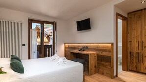 A bedroom with a bed, a wooden desk, a television, and a view of a building outside. - Albergo Alla Posta (Pinzolo)