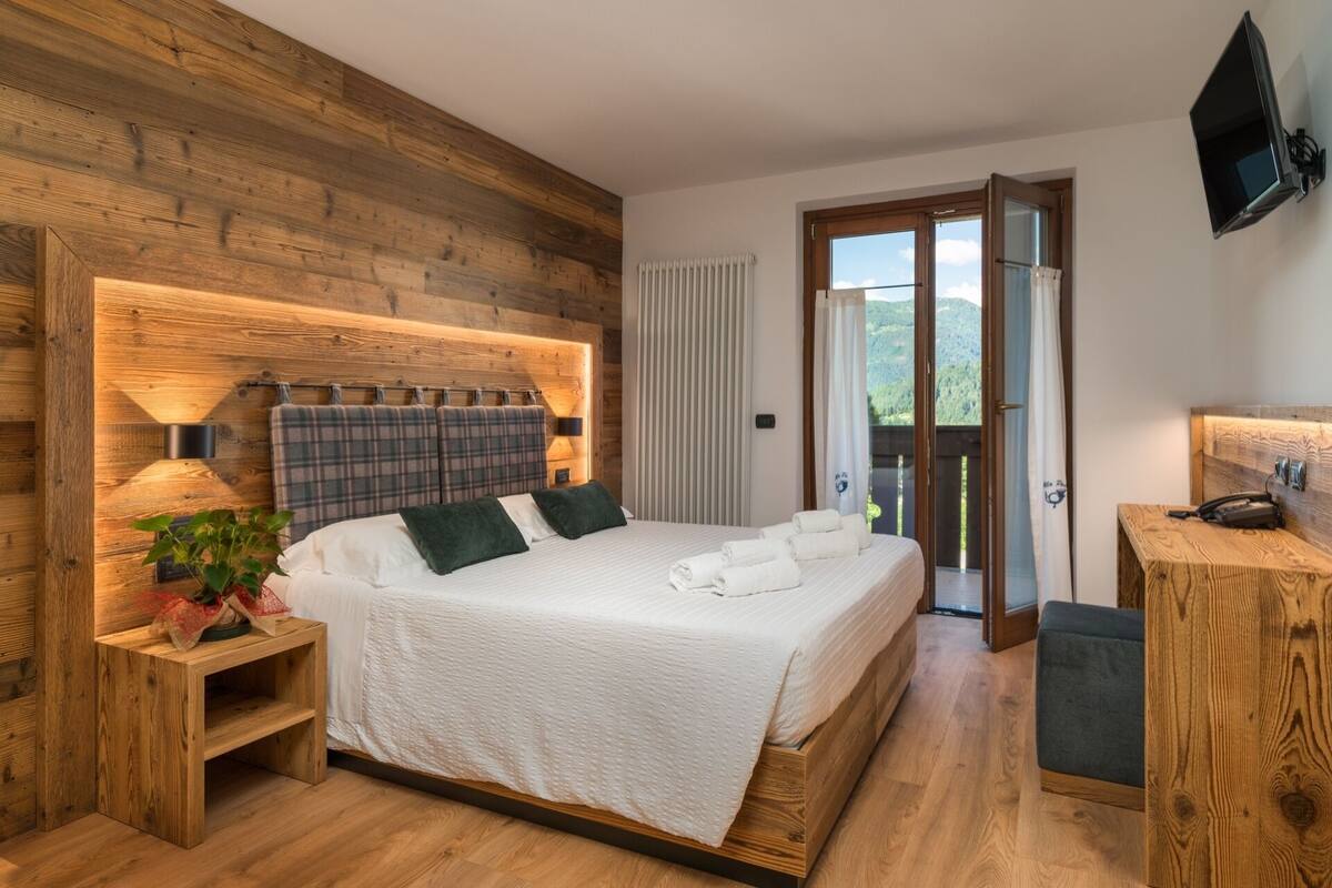 A bedroom with a wooden headboard, a bed with white linens, a bedside table with a lamp, and a view through a glass door to an outdoor area.
