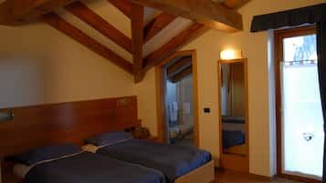 Una camera da letto con due letti, travi in legno al soffitto, un bagno visibile attraverso una porta aperta e una porta scorrevole in vetro che dà sull'esterno.