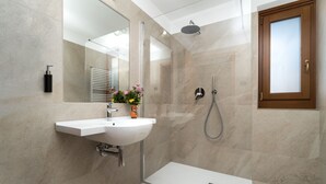 A modern bathroom with a white sink, a glass shower enclosure, and a wooden-framed window. - Albergo Alla Posta (Pinzolo)