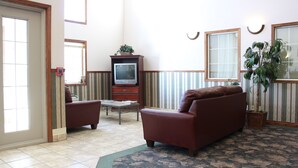 A living room with a brown sofa, a television on a wooden stand, a small table, and a potted plant. - Sunset Inn and Suites (Sioux Lookout)