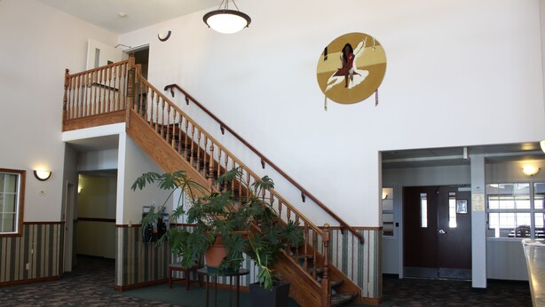 A spacious lobby with a wooden staircase, a large potted plant, and a wall-mounted circular artwork. - Sunset Inn and Suites (Sioux Lookout)