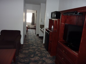 Una habitación de hotel con un sofá marrón oscuro, un mueble de madera con un televisor y una alfombra estampada.