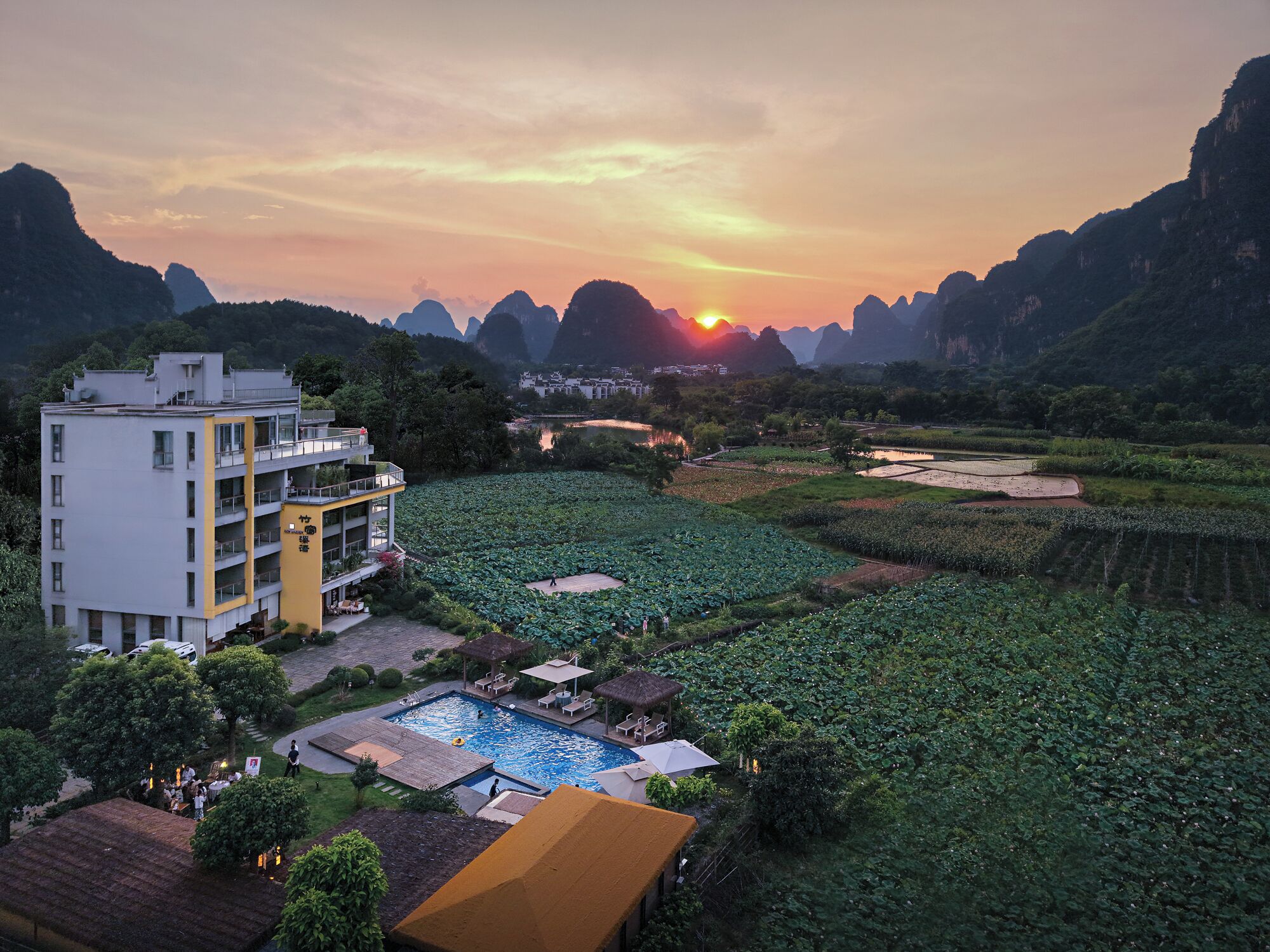 Um hotel com piscina, rodeado por vegetação exuberante e uma vista panorâmica para o pôr do sol.