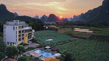 Um hotel com piscina, rodeado por vegetação exuberante e uma vista panorâmica para o pôr do sol.