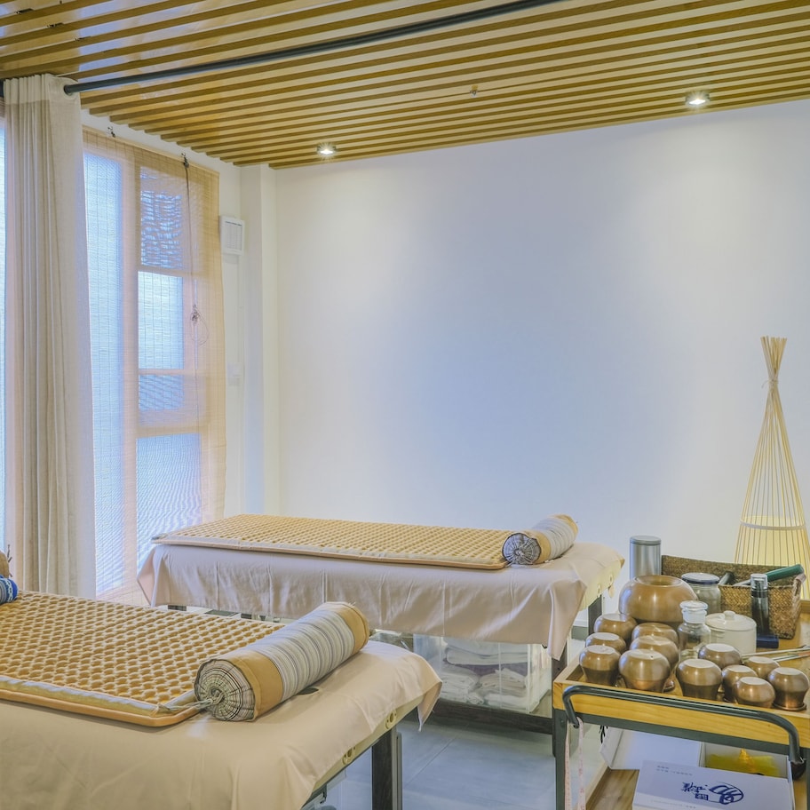 A room with two beds, a small table with tea sets, and a window with curtains.