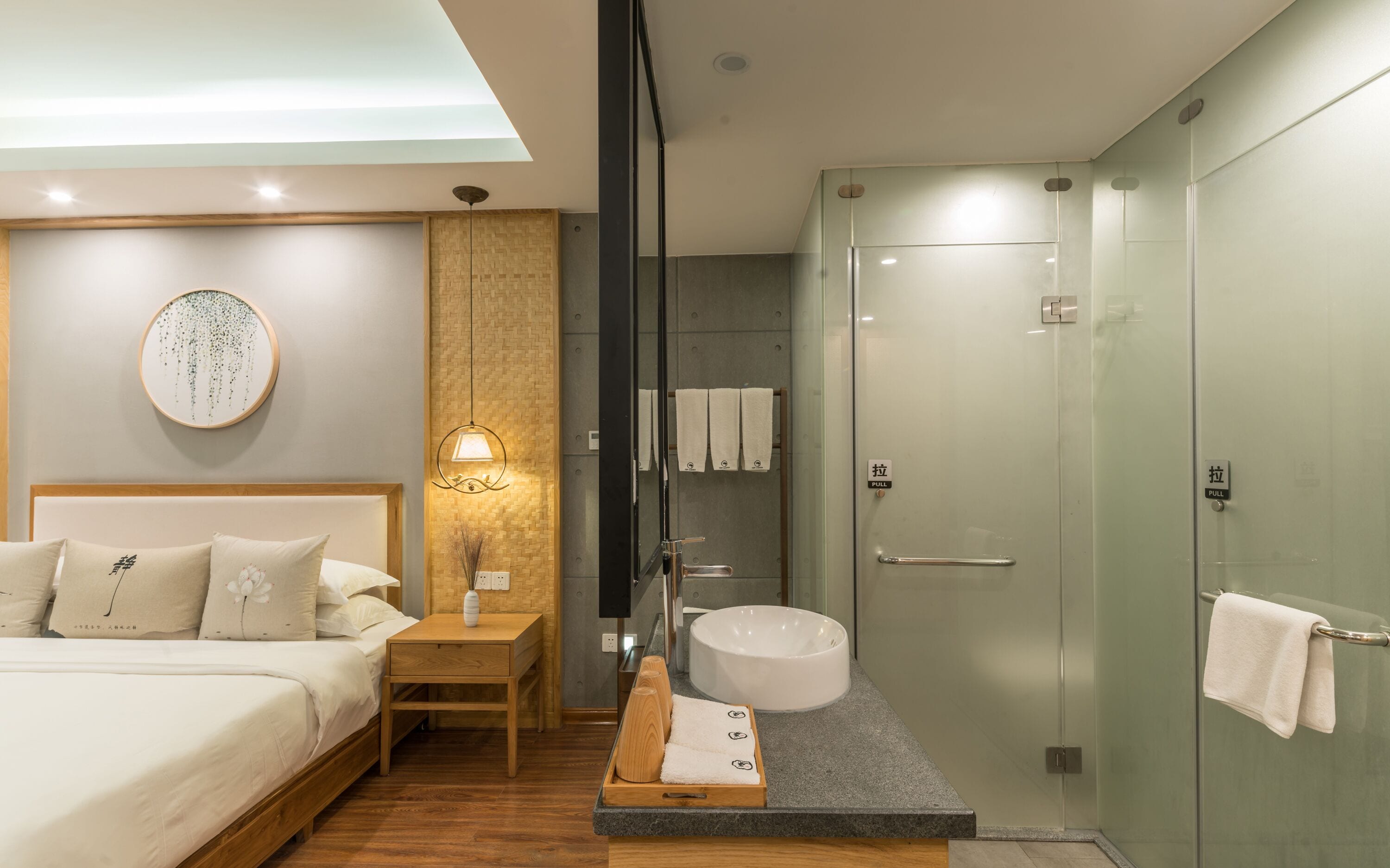 A modern hotel room with a bed, bedside table, and a glass-enclosed shower area.