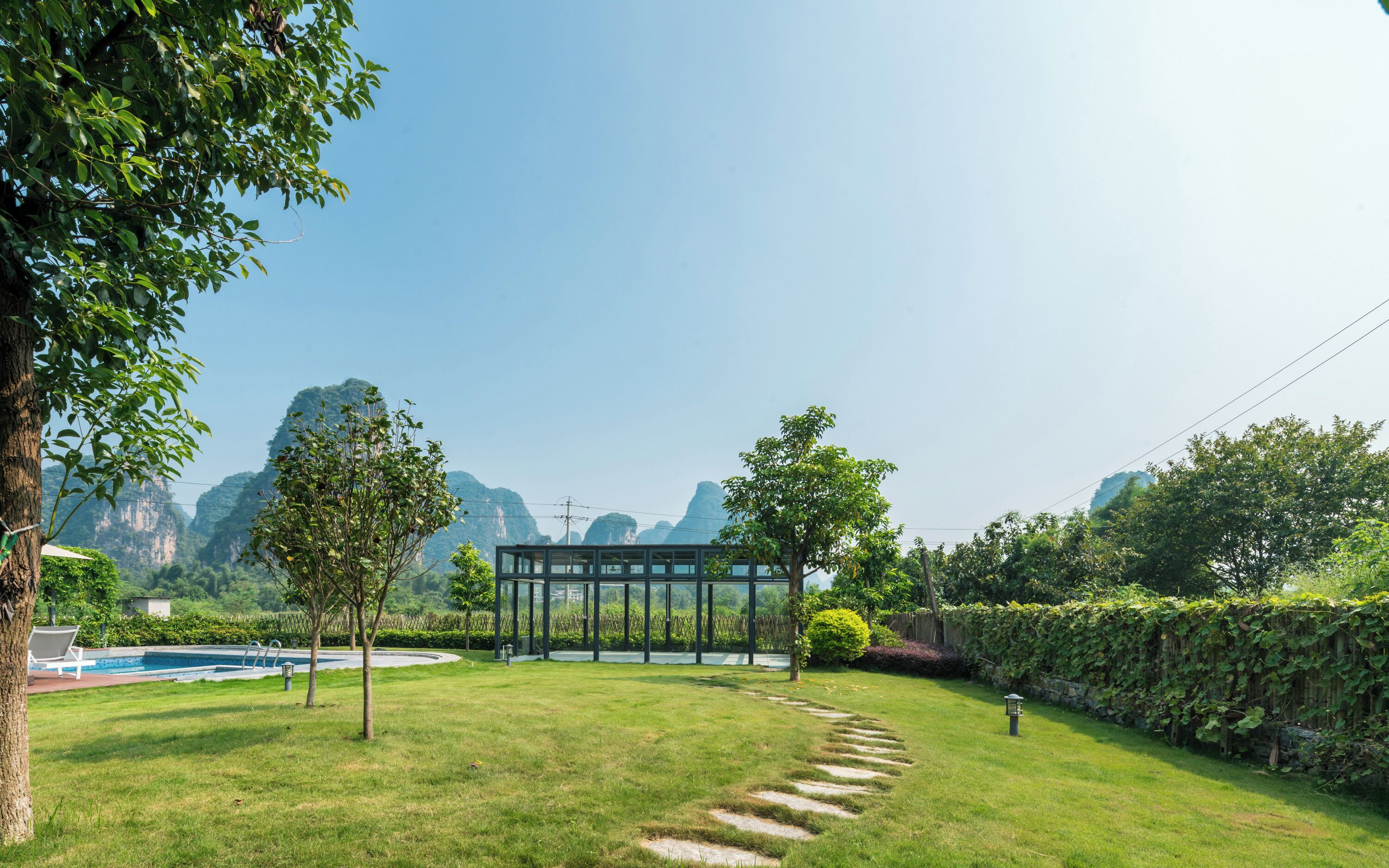 A well-maintained garden with a swimming pool, a glass-enclosed structure, and a stone pathway.