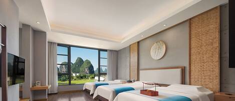 A hotel room with two beds, a TV, a large window with a view of mountains, and a wooden floor.