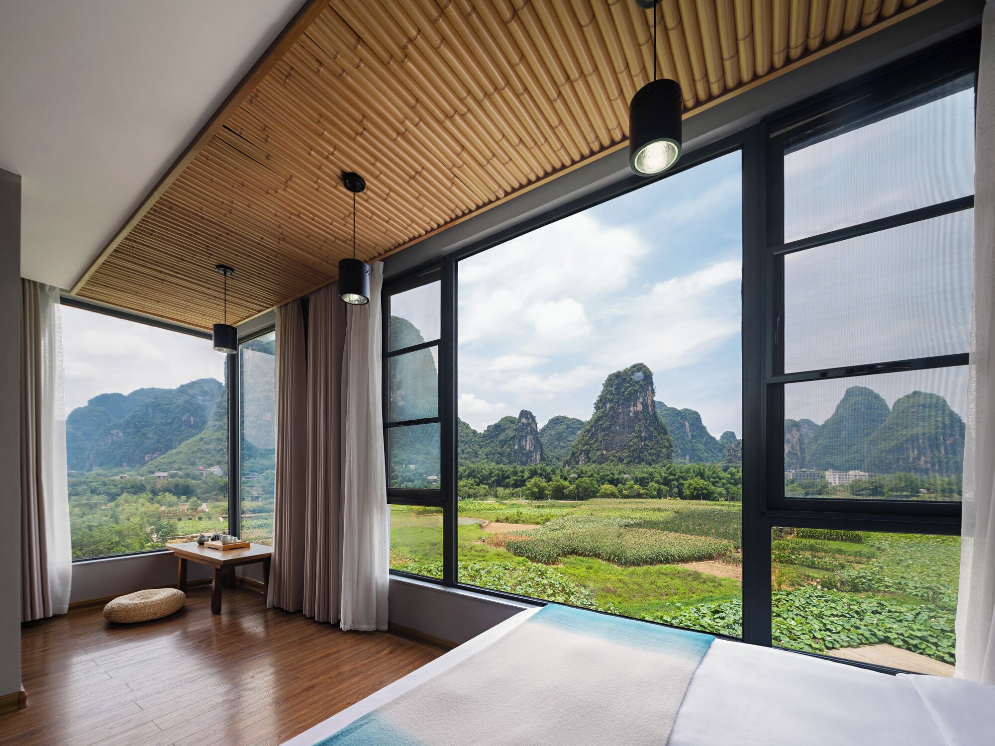 Ein modernes Zimmer mit großen Fenstern, Holzboden und Blick auf eine grüne Landschaft und Berge.