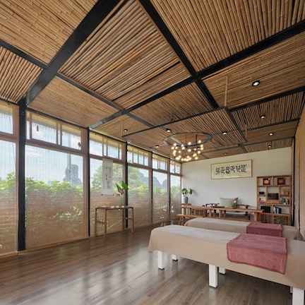 A room with large windows, a wooden ceiling, and a massage table.