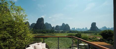A balcony with a wicker sofa, a pool, and a view of karst mountains.