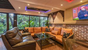 A modern living room with leather sofas, a glass coffee table, and a large TV screen displaying a sports event. - Fair Acres Boutique Hotel (Nairobi)