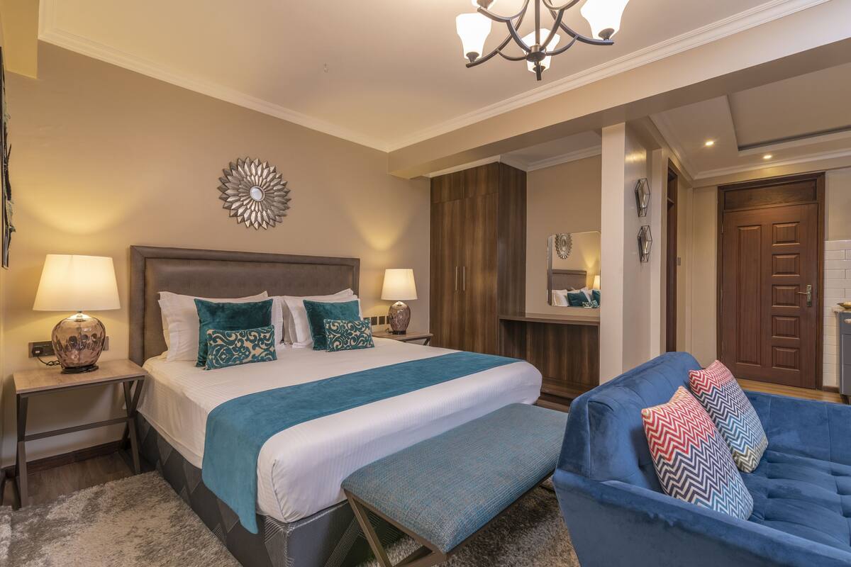 A hotel room with a large bed, a bench, a blue sofa, and a chandelier.