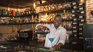 A bartender preparing a drink at a bar with shelves of liquor bottles in the background. - Fair Acres Boutique Hotel (Nairobi)