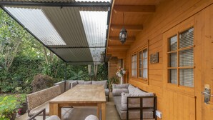 A wooden cabin with a covered patio, a dining table, and seating area. - Fair Acres Boutique Hotel (Nairobi)