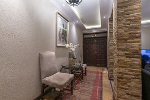 Un couloir avec un mur en pierre, un tableau encadré, une table avec des chaises et une porte portant le numéro 13.