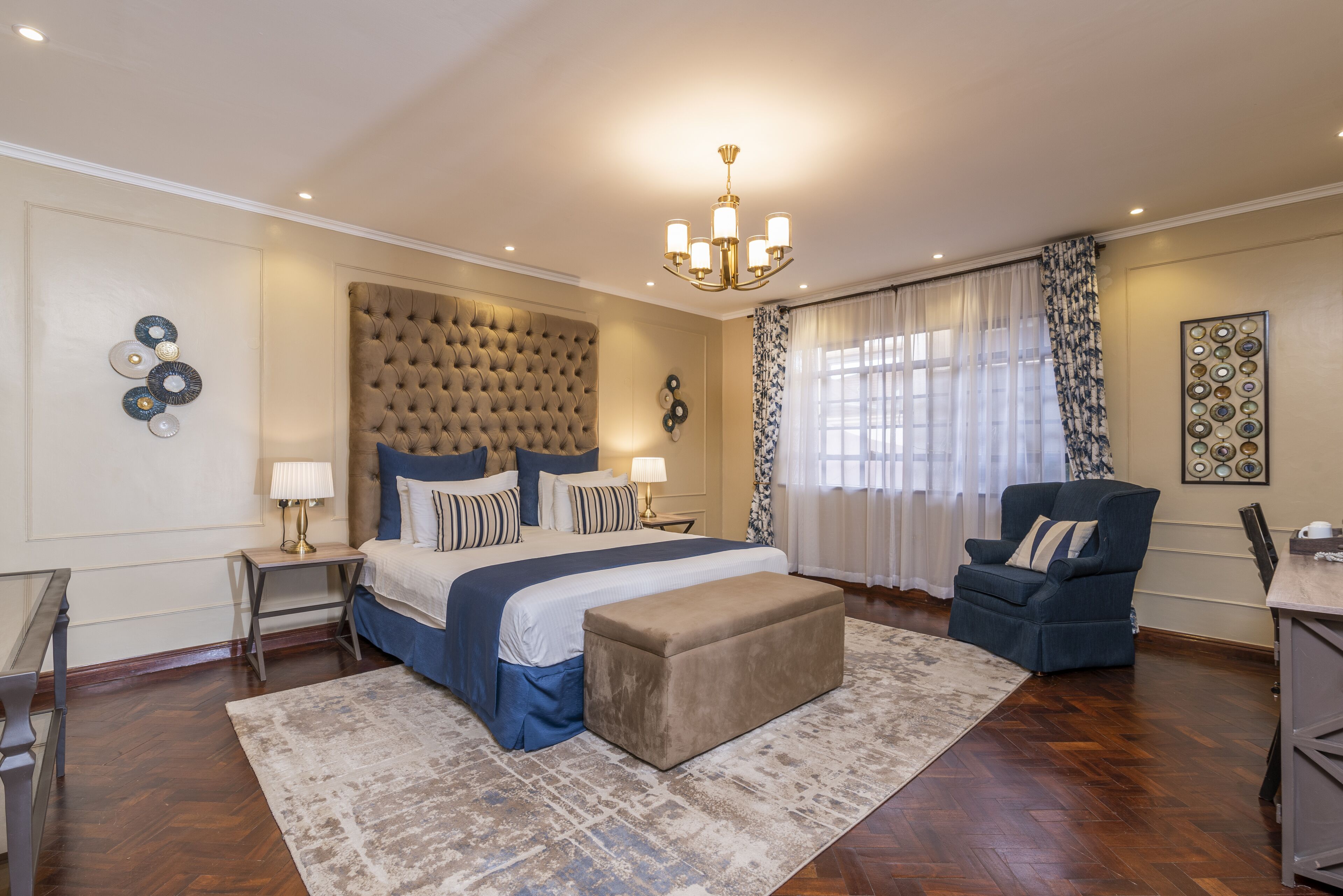 A bedroom with a tufted headboard, a large bed with multiple pillows, a bedside table with a lamp, a chair, and a rug.