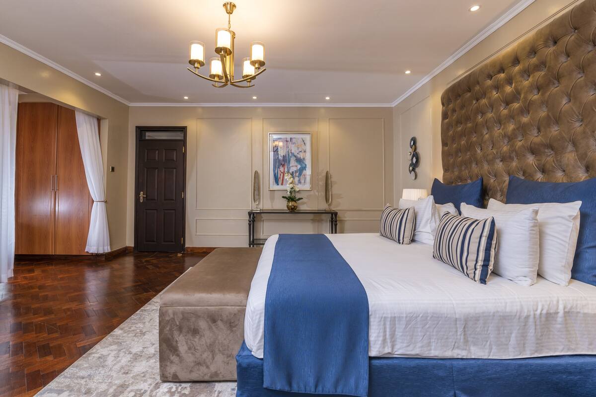 A bedroom with a large bed, a wooden wardrobe, a bench, and a chandelier.