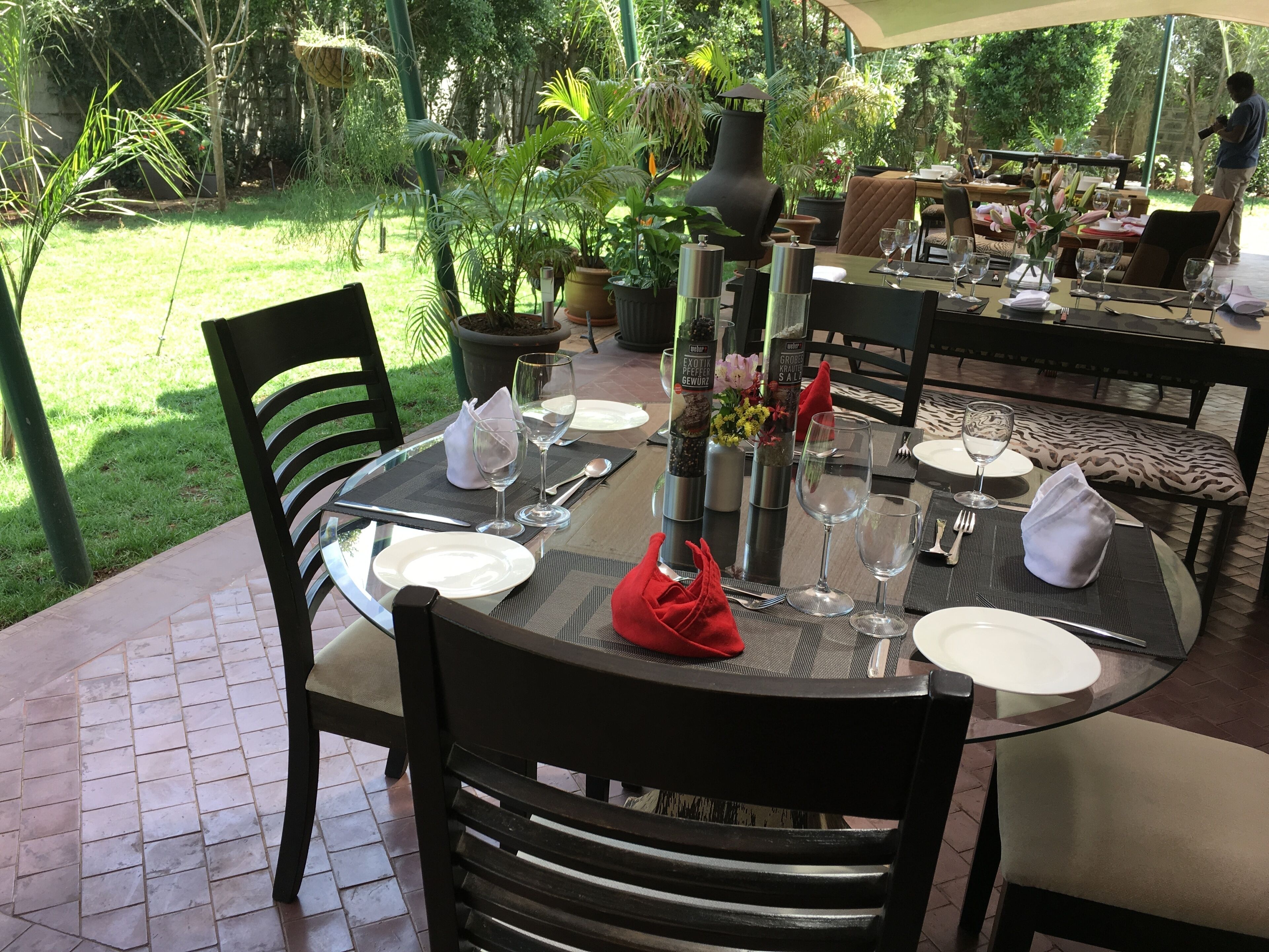 A dining table set outdoors with chairs, a vase with flowers, and a view of a garden.