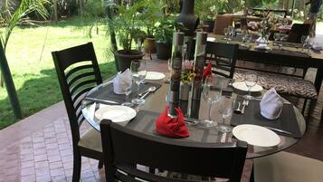 A dining table set outdoors with chairs, a vase with flowers, and a view of a garden.