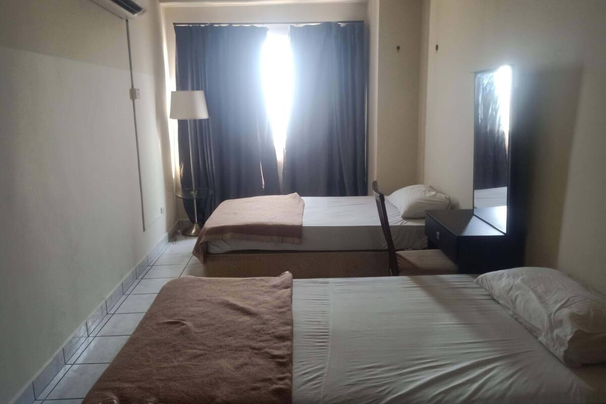 A hotel room with two beds, a lamp, a mirror, and a window with curtains.