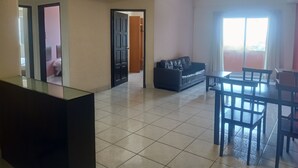 A spacious living area with a tiled floor, a dark leather sofa, a dining table with chairs, and a ceiling fan. - Globallon Hotel Apartment (Malacca City)