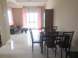 A dining area with a table and chairs, a sofa, and a window with curtains. - Globallon Hotel Apartment (Malacca City)