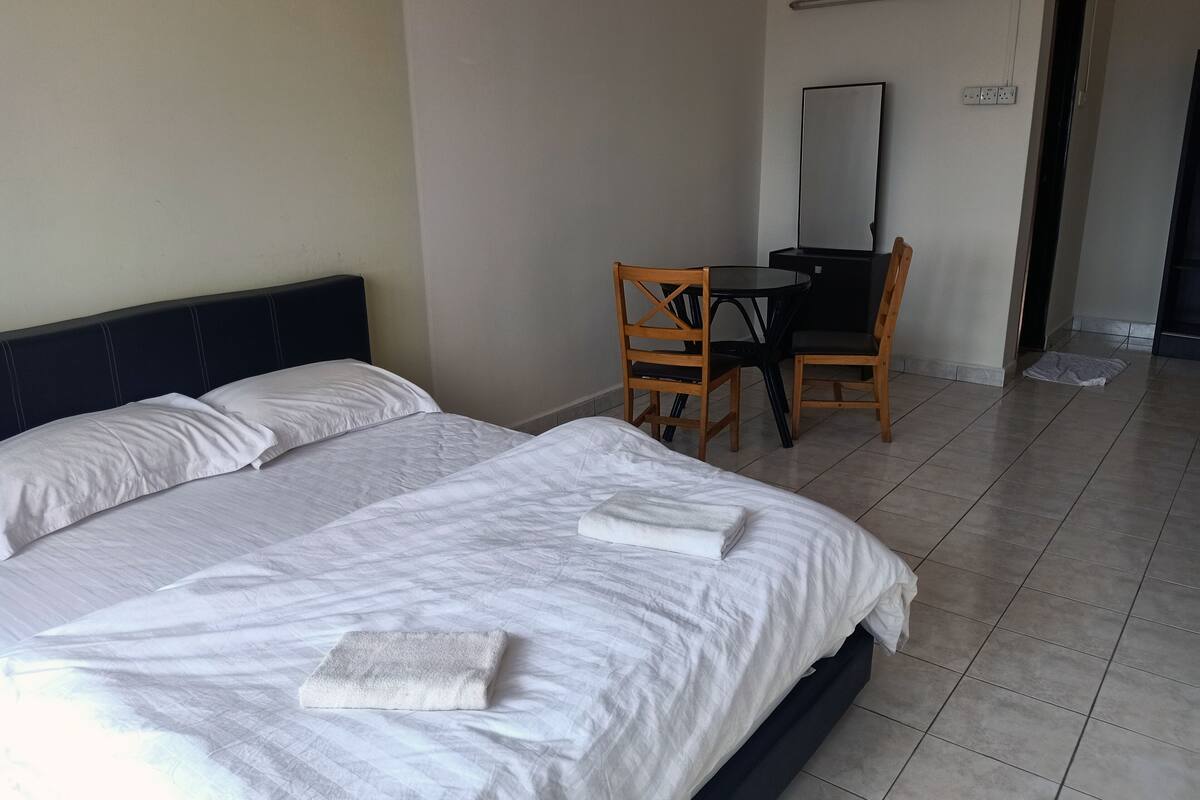 A hotel room with two single beds, a small round table with two chairs, a desk, and a mirror.