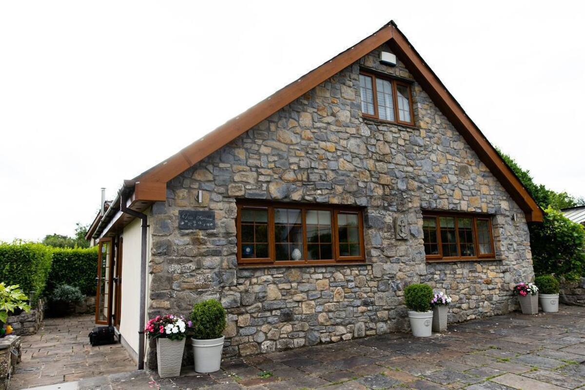 A stone building with a sloped roof, two windows with wooden frames, and potted plants in front.