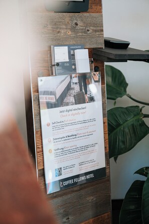 Un comptoir d’accueil d’hôtel avec un panneau numérique indiquant l’enregistrement, un comptoir en bois et une plante en arrière-plan.