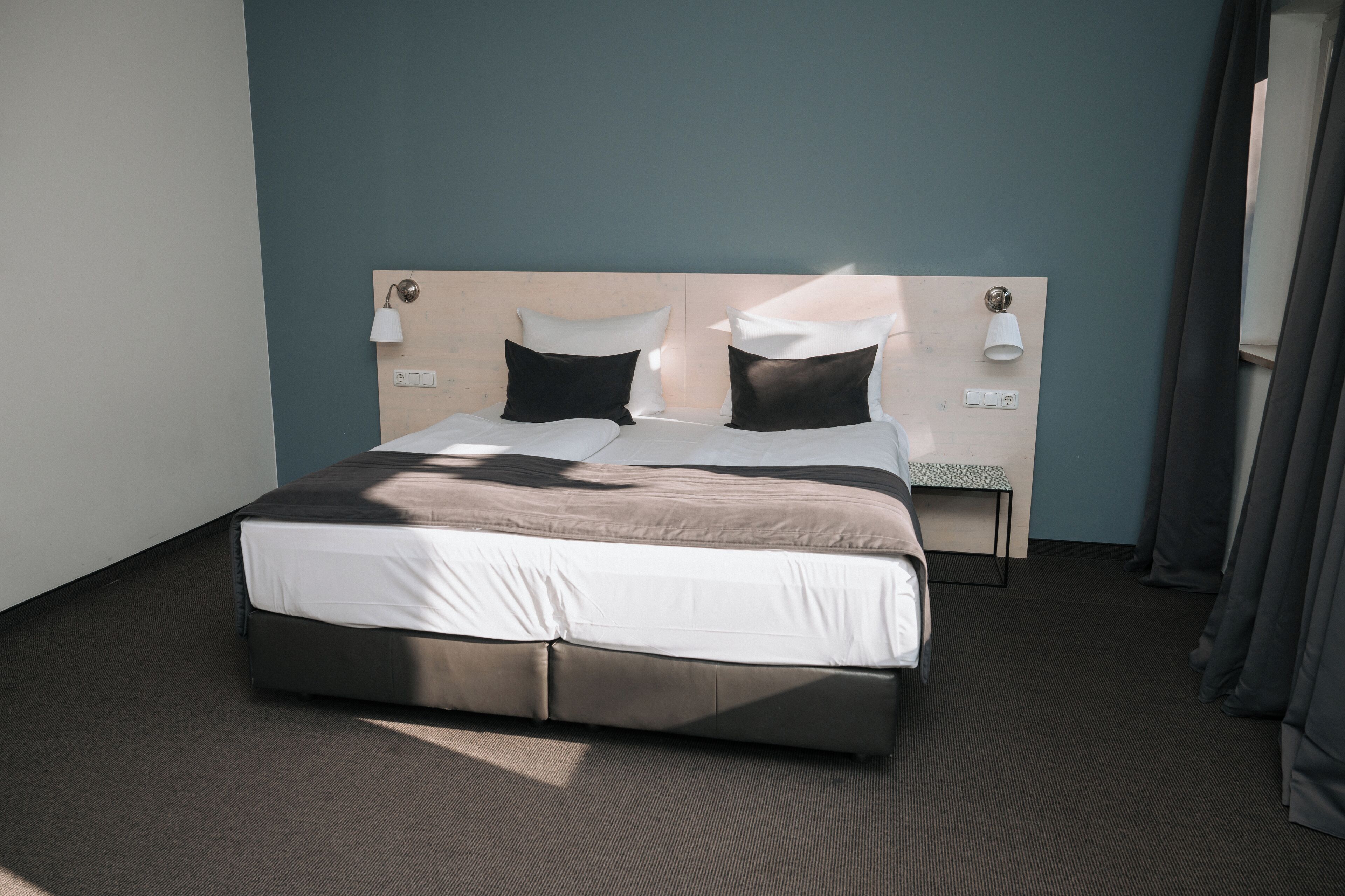 A modern hotel room with a large bed, two bedside lamps, a small table, and a headboard with built-in lighting.