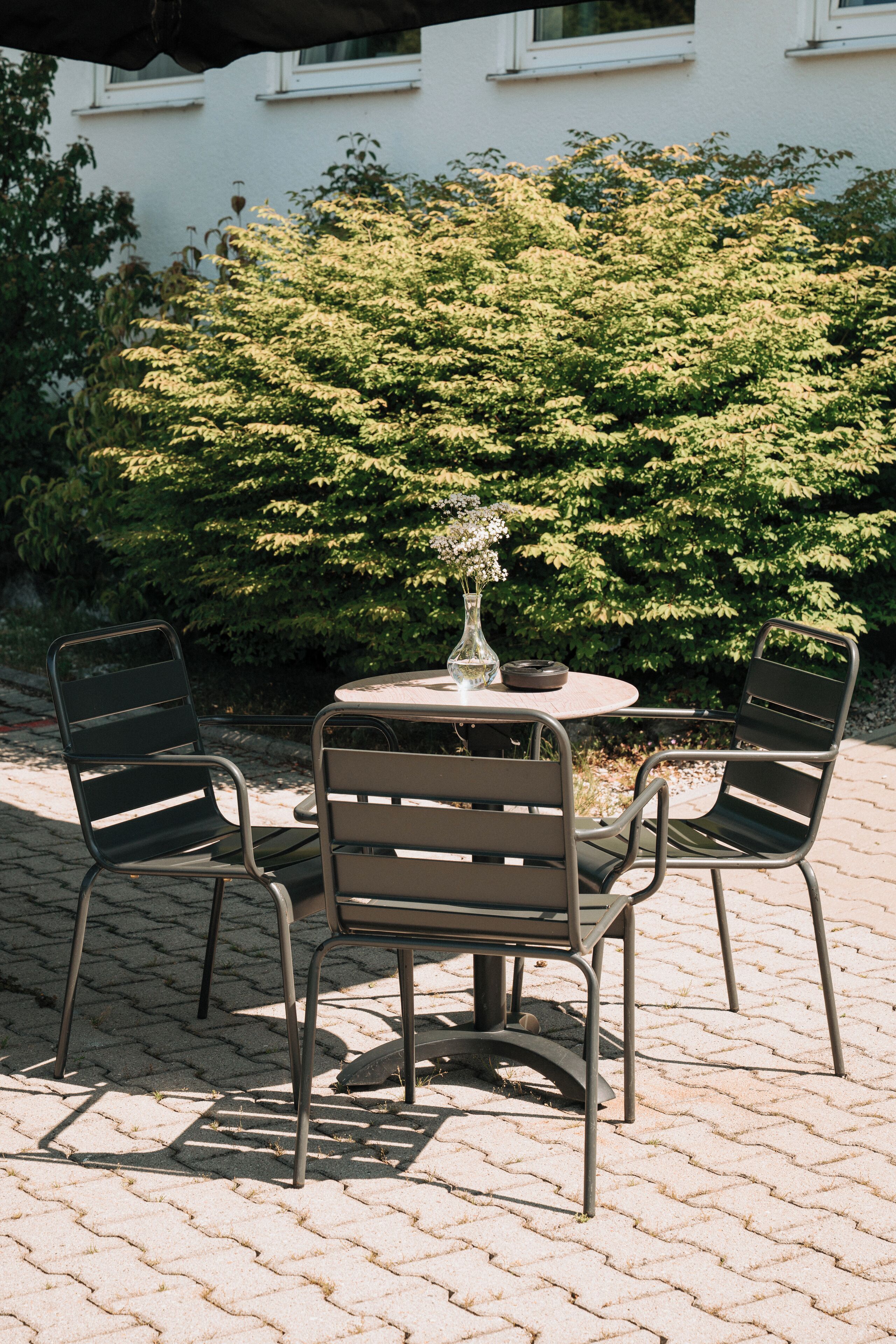 A round metal table with four chairs, a vase with flowers, and a plate.