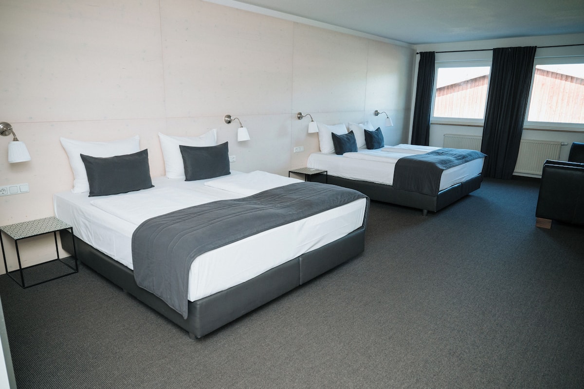A hotel room with two beds, a small table, and a chair.