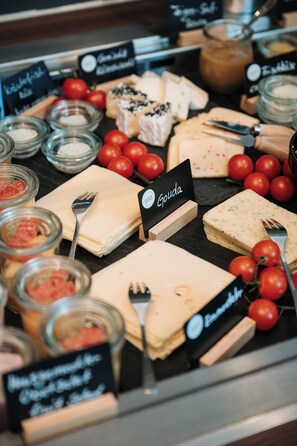Un plateau de fromages comprenant différents types de fromages, des tomates et des condiments.