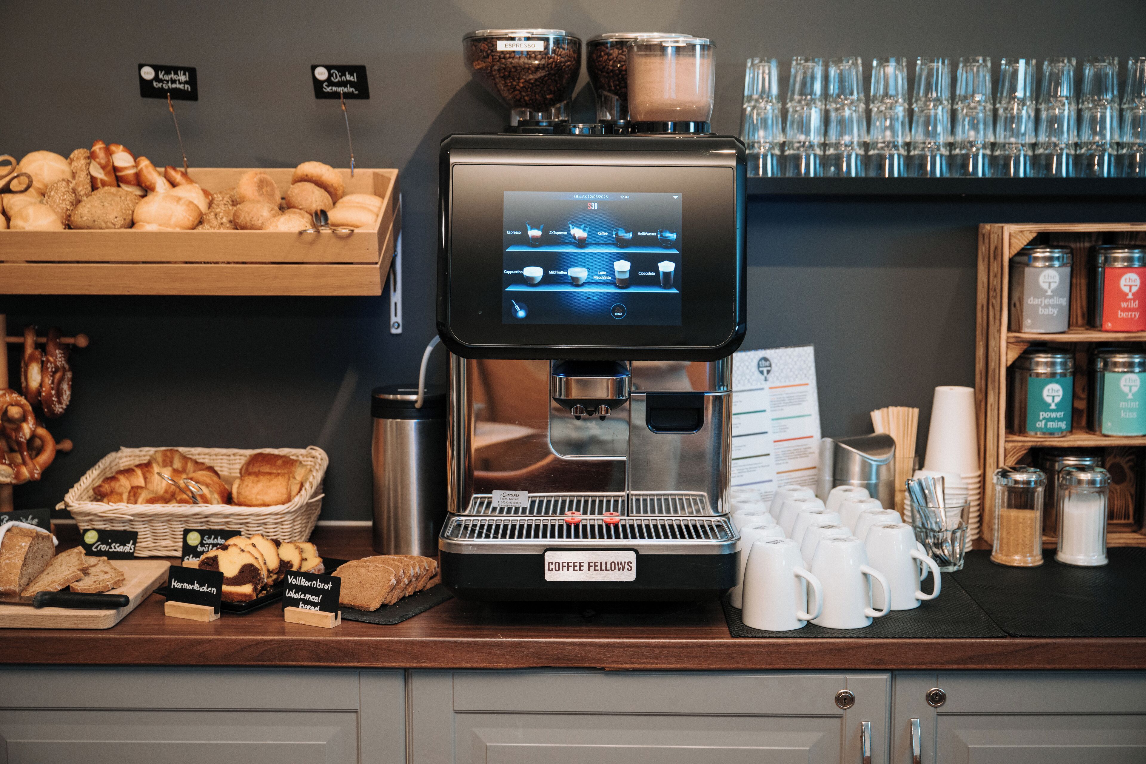 A coffee machine with a digital display, a coffee menu, and various baked goods on display.