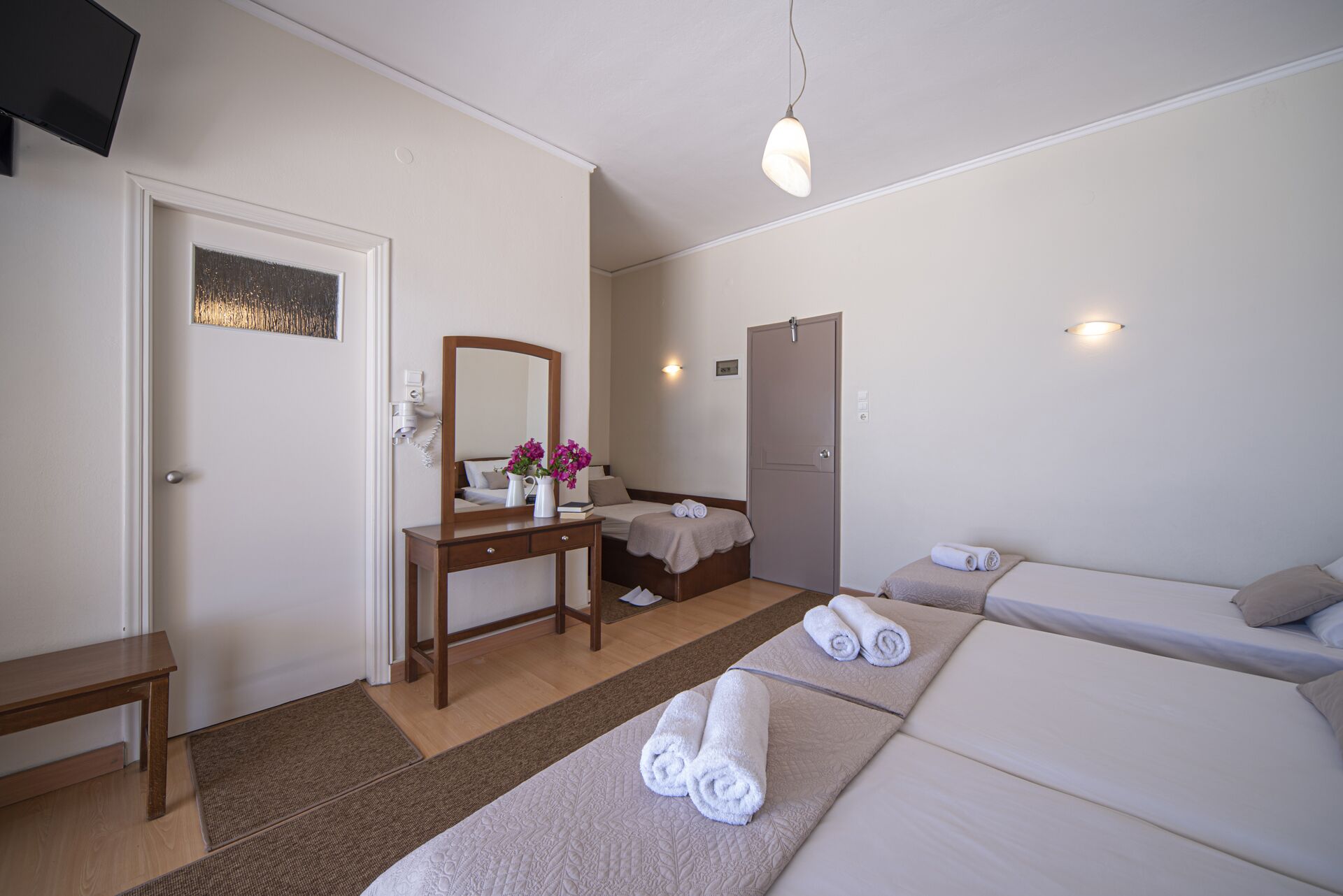 Habitación de hotel con cama, escritorio con espejo, mesita de noche, puerta y una pequeña zona de estar.
