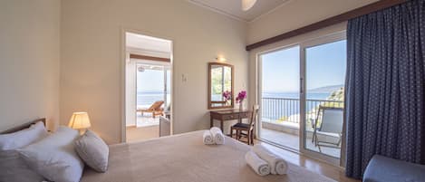 A hotel room with a large bed, a desk with a chair, a mirror, and a view of the sea.